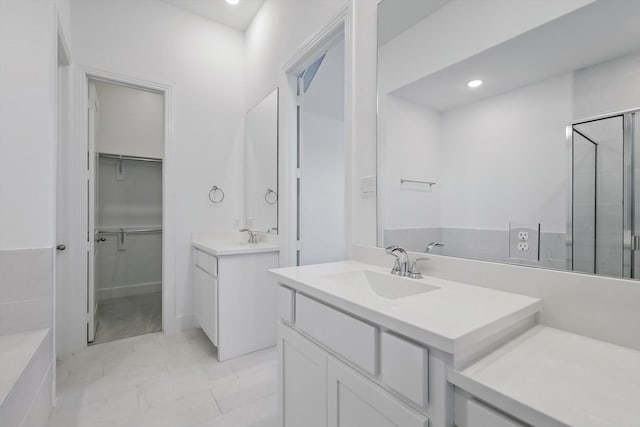 bathroom featuring recessed lighting, a spacious closet, a sink, a stall shower, and two vanities