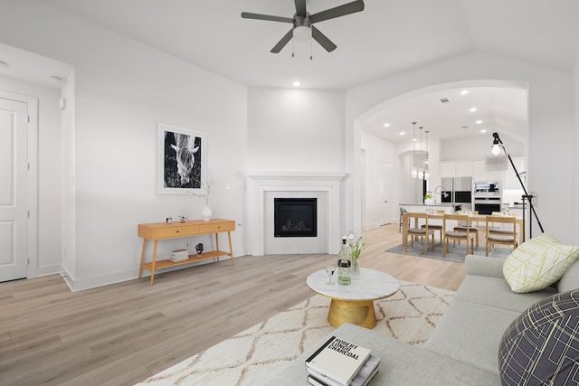 living area with light wood finished floors, arched walkways, recessed lighting, and a ceiling fan
