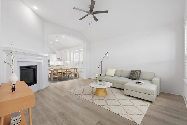 living area featuring vaulted ceiling, light wood-type flooring, arched walkways, and a ceiling fan