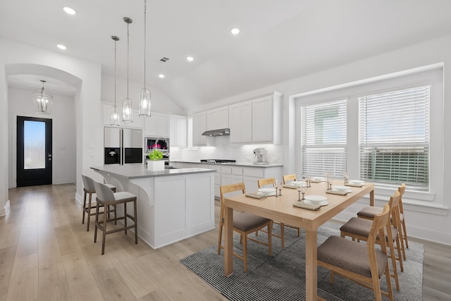 kitchen featuring decorative backsplash, refrigerator with ice dispenser, cooktop, under cabinet range hood, and a center island