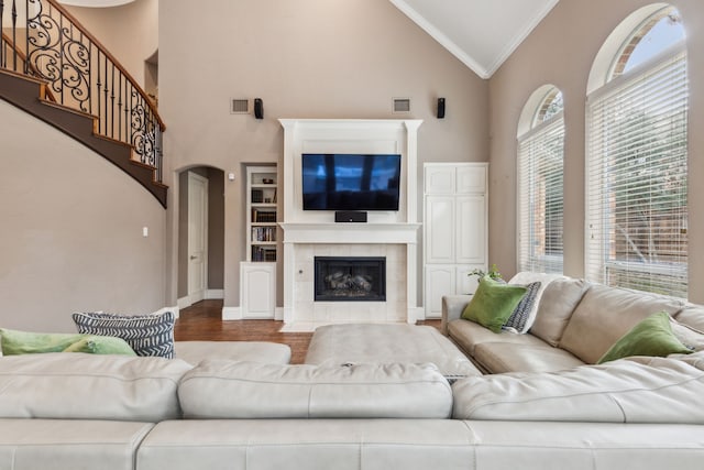 living room featuring arched walkways, high vaulted ceiling, a tile fireplace, visible vents, and ornamental molding