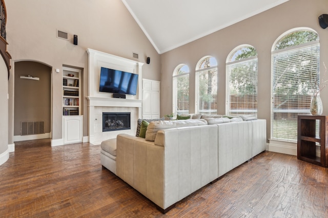 living area with arched walkways, built in shelves, a fireplace, visible vents, and dark wood-style floors