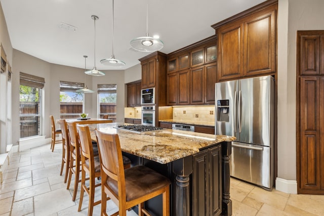 kitchen featuring light stone counters, stone tile floors, a kitchen island, appliances with stainless steel finishes, and tasteful backsplash