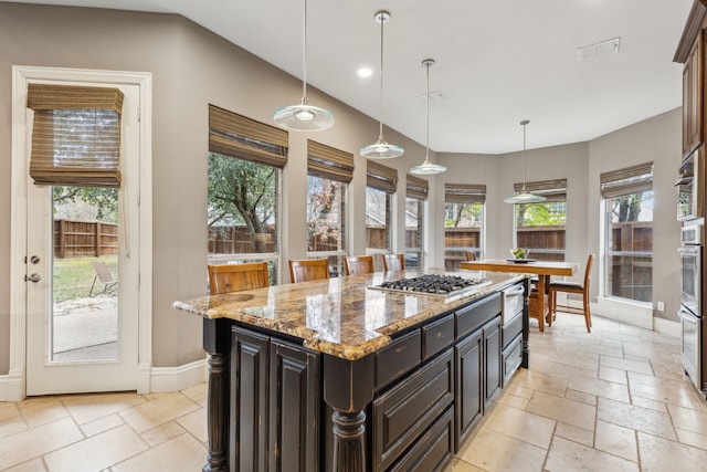 kitchen featuring baseboards, light stone counters, stone tile flooring, stainless steel gas stovetop, and pendant lighting