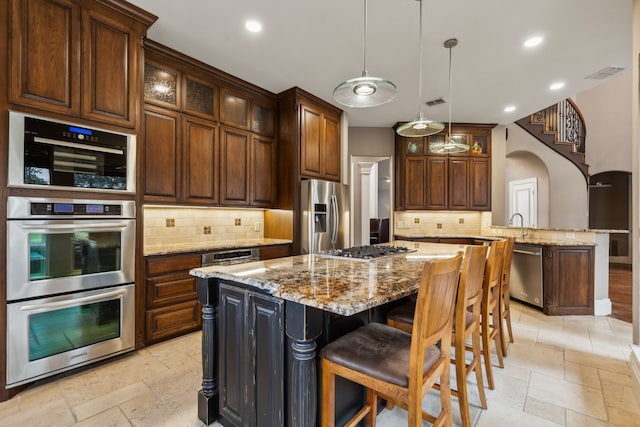 kitchen with light stone counters, arched walkways, stone tile floors, appliances with stainless steel finishes, and glass insert cabinets