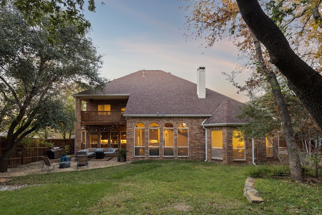 rear view of house featuring brick siding, outdoor lounge area, a lawn, fence, and a balcony