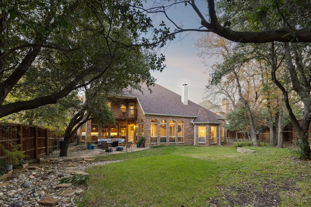 back of house at dusk featuring a lawn, a fenced backyard, a chimney, an outdoor hangout area, and a patio area