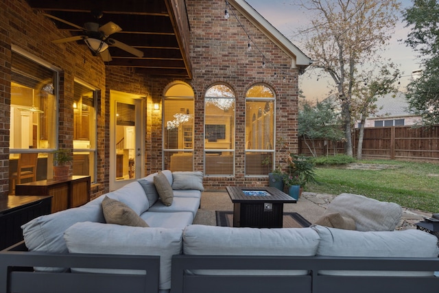 patio terrace at dusk with fence, a ceiling fan, and an outdoor living space with a fire pit