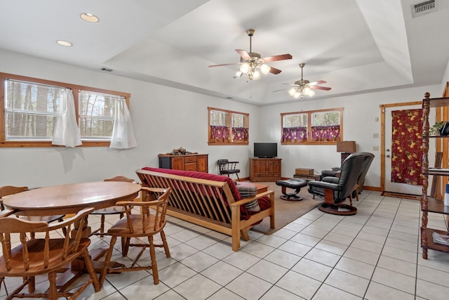 living room with a tray ceiling, light tile patterned floors, recessed lighting, visible vents, and baseboards