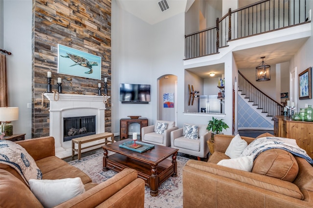 living room featuring arched walkways, a fireplace, visible vents, stairway, and a towering ceiling