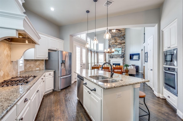 kitchen with a fireplace, stainless steel appliances, custom range hood, visible vents, and a sink