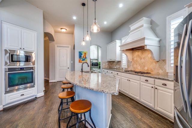 kitchen with arched walkways, stainless steel appliances, premium range hood, a sink, and white cabinets