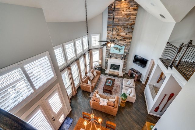 living room featuring visible vents, a ceiling fan, a stone fireplace, wood finished floors, and high vaulted ceiling