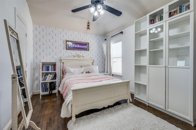 bedroom featuring dark wood finished floors, an accent wall, ceiling fan, baseboards, and wallpapered walls