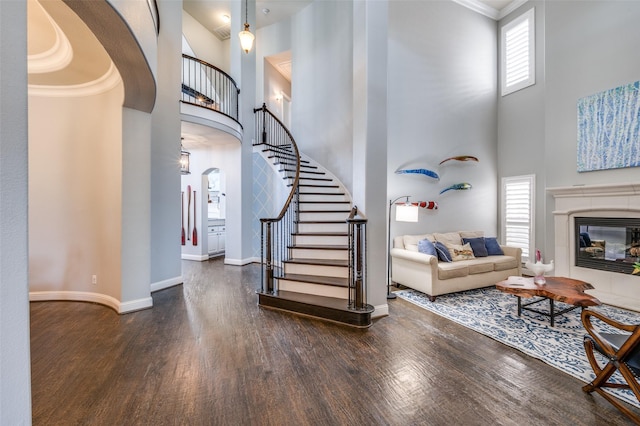 interior space featuring a fireplace, a towering ceiling, wood finished floors, baseboards, and stairs