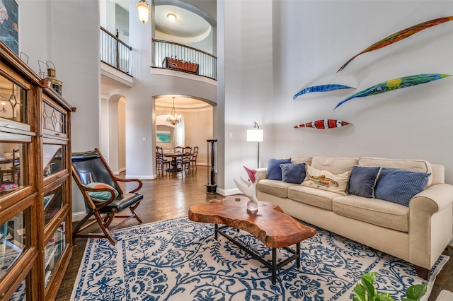 living area featuring arched walkways, a chandelier, a high ceiling, wood finished floors, and baseboards