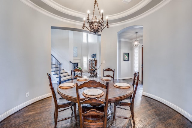 dining area featuring arched walkways, a raised ceiling, wood finished floors, a chandelier, and baseboards