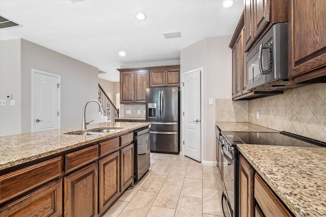 kitchen featuring appliances with stainless steel finishes, decorative backsplash, a sink, and light stone countertops