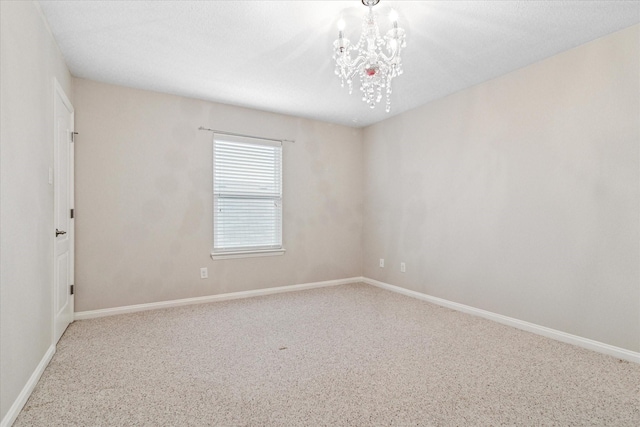 carpeted spare room featuring baseboards and an inviting chandelier