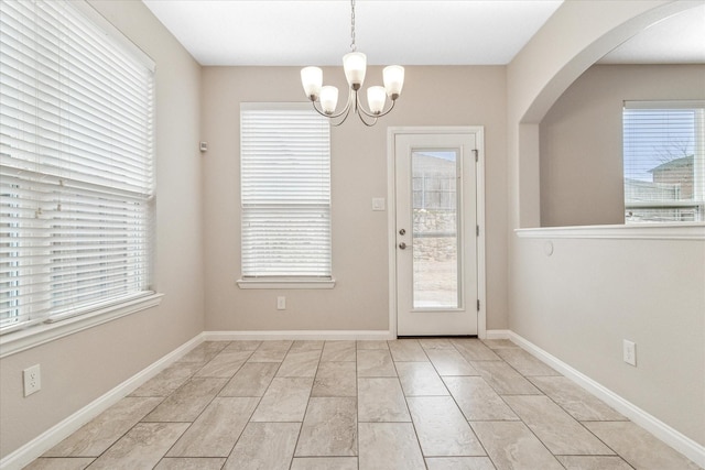 doorway to outside featuring arched walkways, a notable chandelier, plenty of natural light, and baseboards