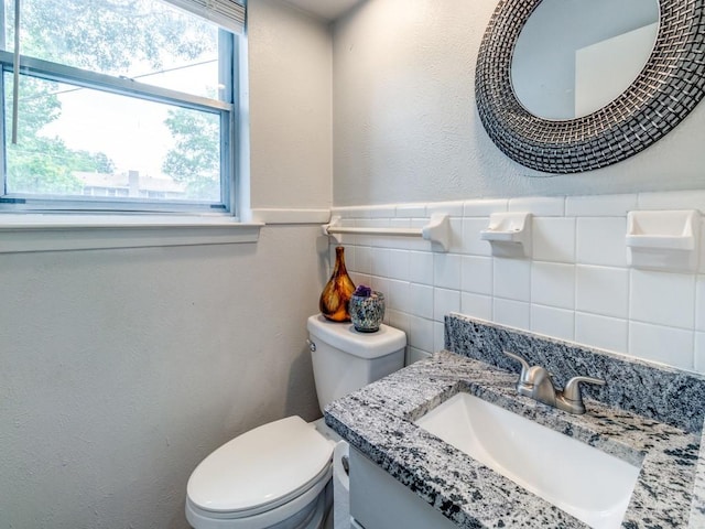 half bathroom with a textured wall, toilet, vanity, tile walls, and wainscoting