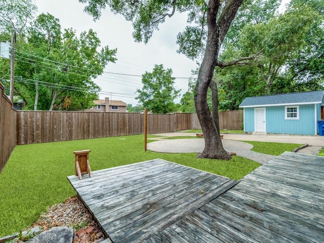 wooden terrace with an outbuilding, a patio area, a fenced backyard, and a lawn