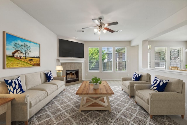 living area with ceiling fan, visible vents, a tiled fireplace, and wood finished floors