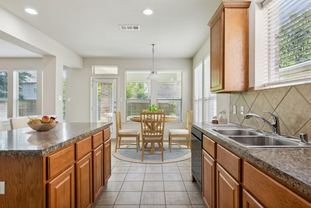 kitchen featuring light tile patterned floors, decorative backsplash, brown cabinetry, dark countertops, and a sink