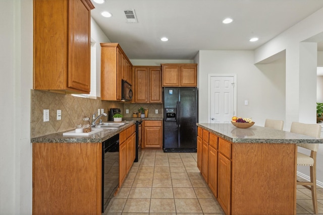 kitchen featuring a sink, visible vents, a center island, black appliances, and a kitchen bar