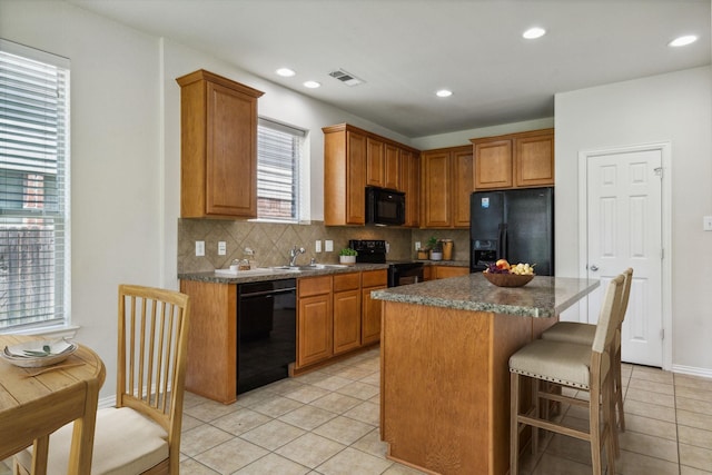 kitchen with visible vents, a breakfast bar area, a sink, black appliances, and backsplash