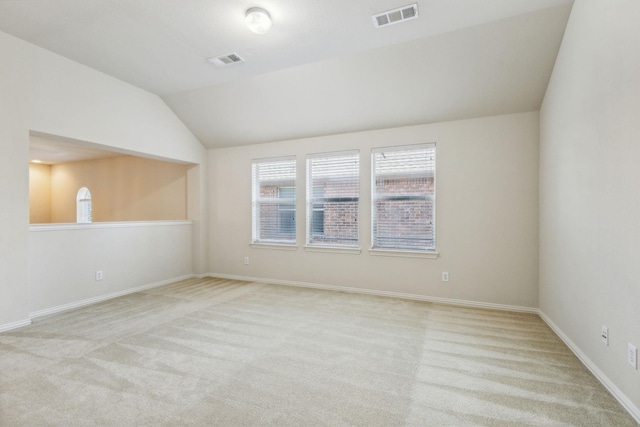 carpeted empty room featuring vaulted ceiling and visible vents