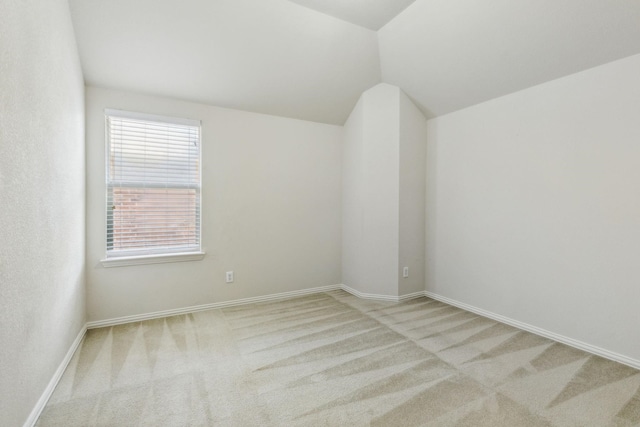 carpeted spare room featuring vaulted ceiling and baseboards