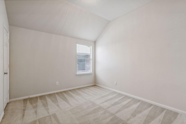 spare room with light carpet, baseboards, and vaulted ceiling