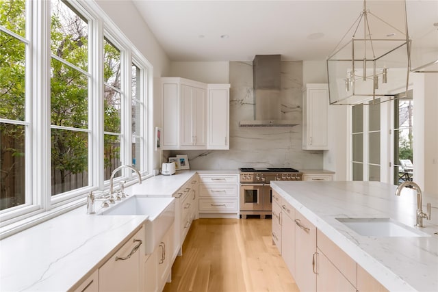 kitchen featuring wall chimney range hood, range with two ovens, a sink, and decorative backsplash