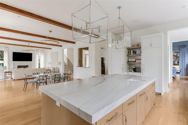 kitchen with a kitchen island with sink, light wood-type flooring, a fireplace, open shelves, and a sink