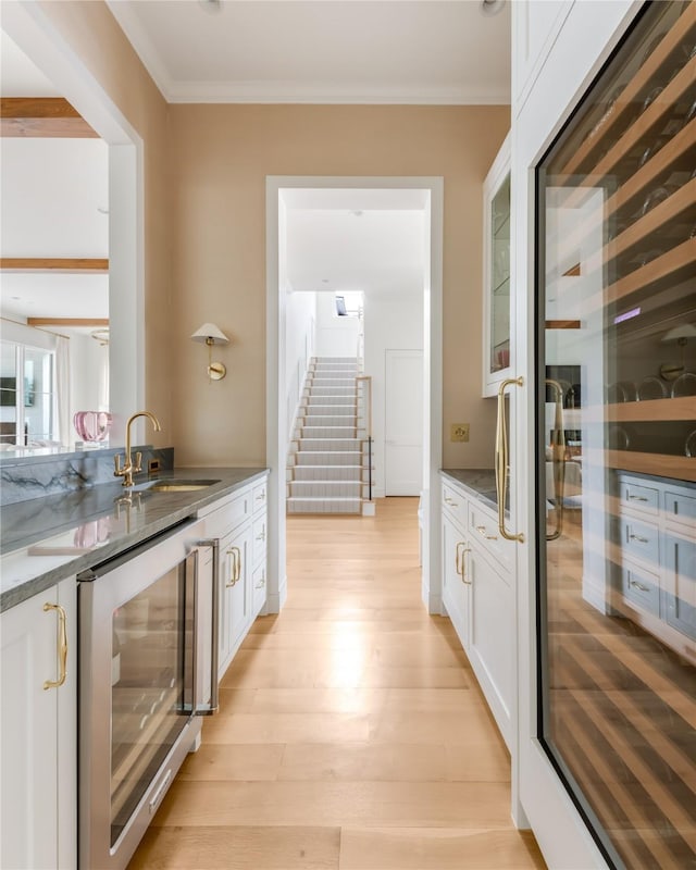 bar featuring light wood-style flooring, wine cooler, stairway, ornamental molding, and a sink