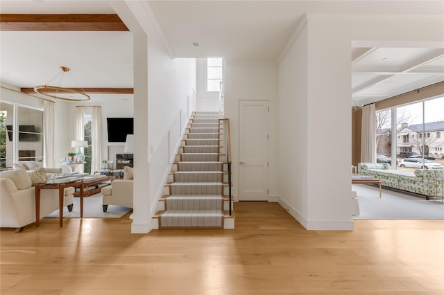 stairs featuring ornamental molding, a wealth of natural light, beamed ceiling, and wood finished floors