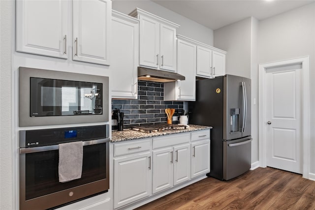 kitchen with backsplash, appliances with stainless steel finishes, dark wood-type flooring, white cabinets, and under cabinet range hood