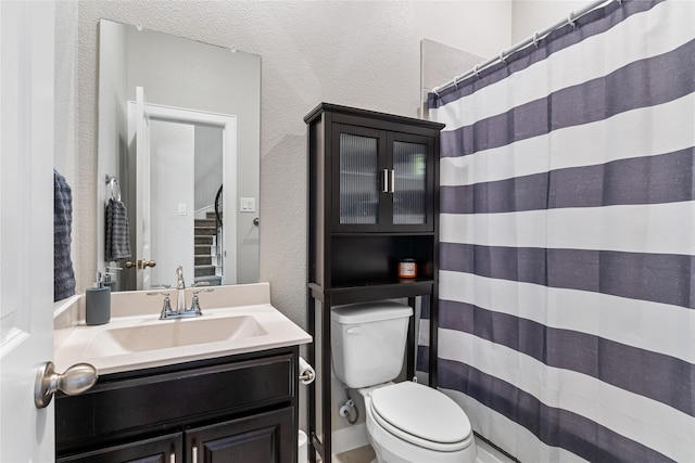 full bathroom with a textured wall, a shower with shower curtain, vanity, and toilet