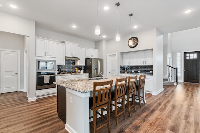 kitchen featuring a center island with sink, appliances with stainless steel finishes, a kitchen breakfast bar, wood finished floors, and a sink