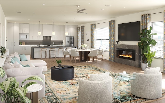 living room featuring a glass covered fireplace, wood finished floors, a healthy amount of sunlight, and a ceiling fan