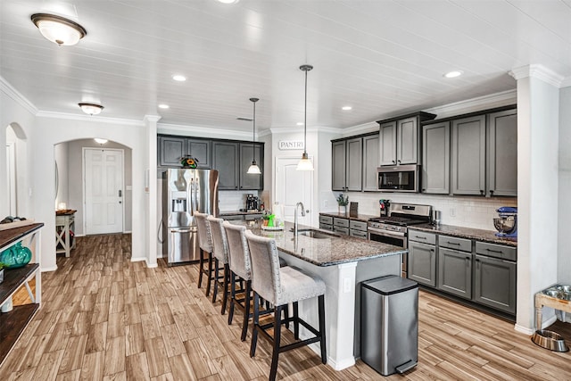 kitchen featuring arched walkways, dark stone counters, appliances with stainless steel finishes, a kitchen bar, and a sink