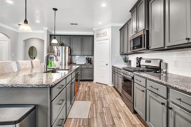 kitchen featuring dark stone counters, an island with sink, appliances with stainless steel finishes, ornamental molding, and a sink