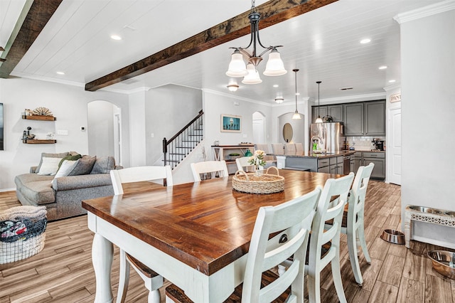 dining space with light wood-style flooring, arched walkways, beamed ceiling, and stairway