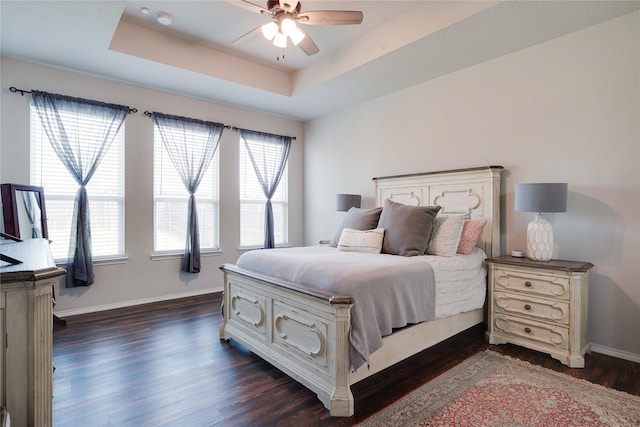 bedroom with baseboards, a tray ceiling, dark wood finished floors, and a ceiling fan