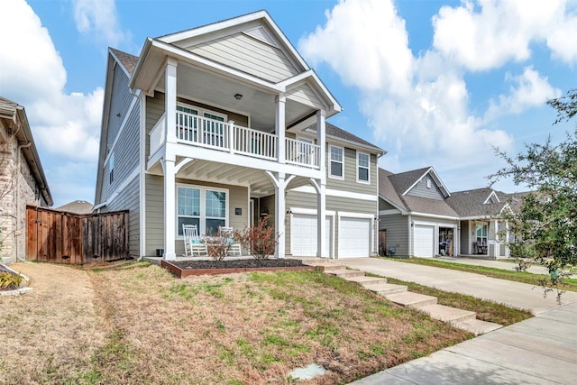 traditional-style house featuring covered porch, a balcony, a garage, driveway, and a front lawn