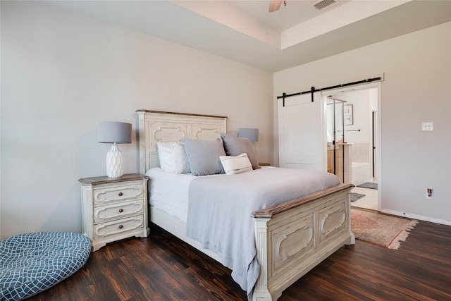 bedroom featuring wood finished floors, connected bathroom, baseboards, and a barn door