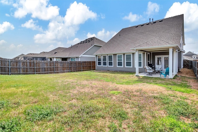 back of property with a patio, a yard, a shingled roof, and a fenced backyard