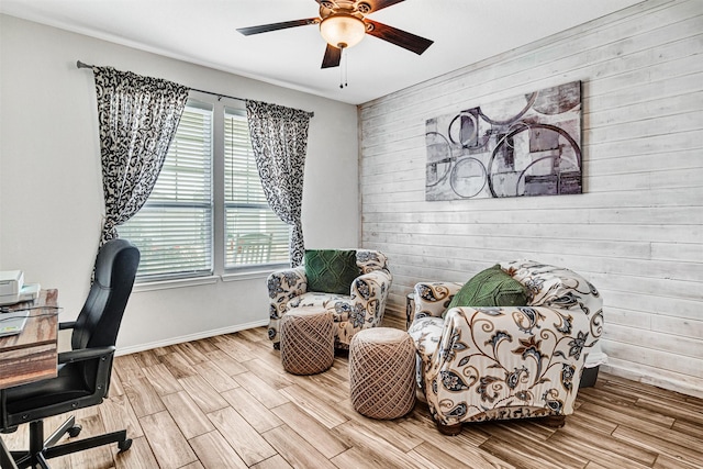 office area with a ceiling fan, wood walls, baseboards, and wood finished floors