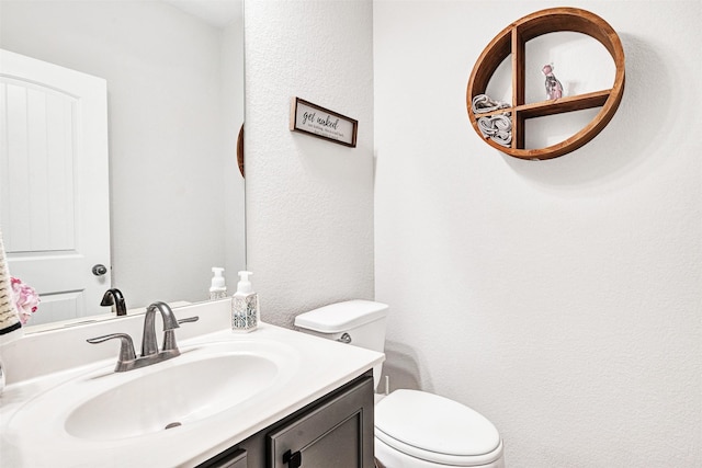 bathroom featuring a textured wall, vanity, and toilet